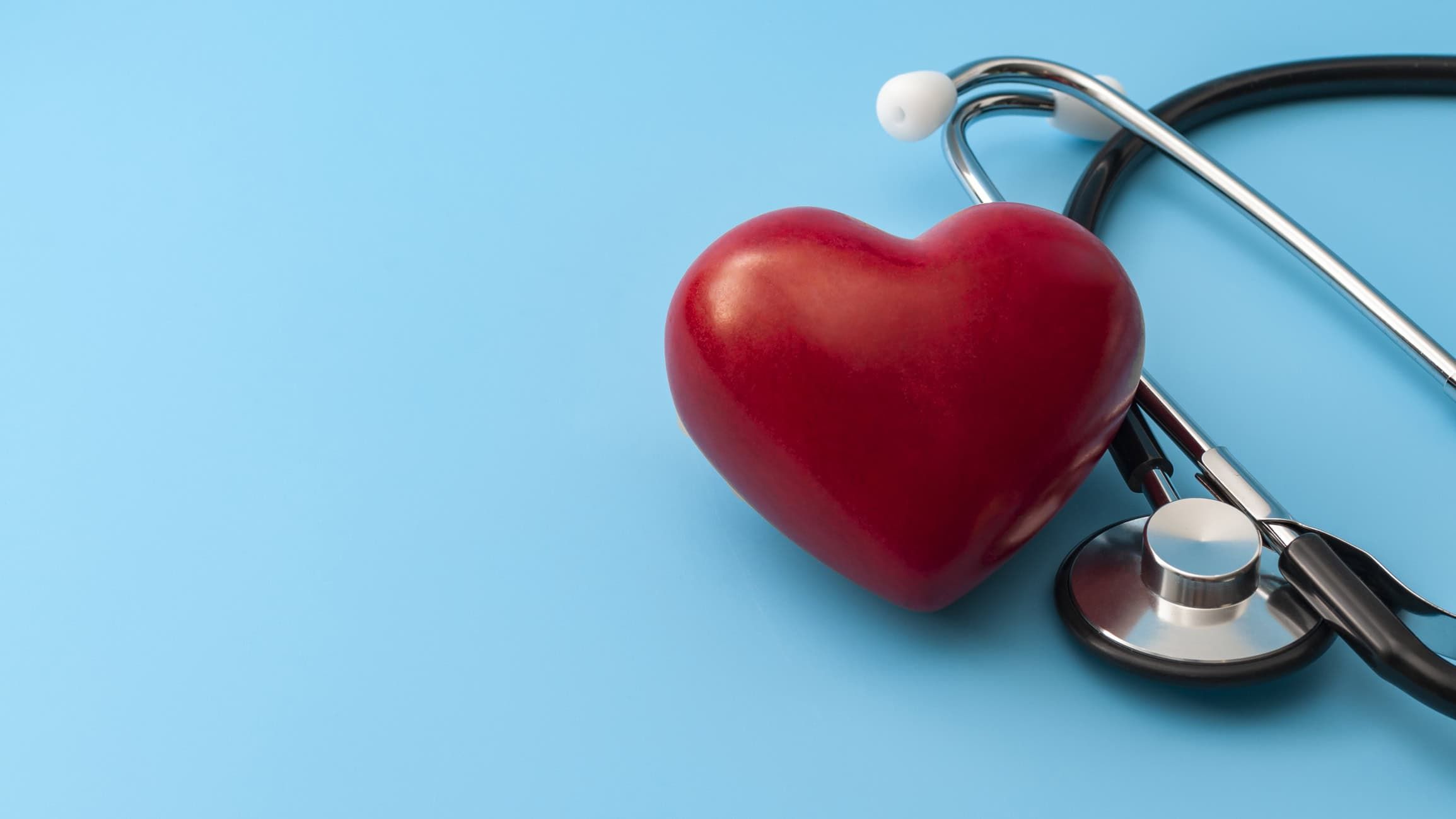 Red heart-shaped object with stethoscope on light blue background for cardiac health concept