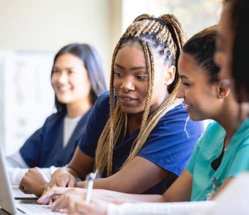 Diverse nursing students studying together with laptop in medical education classroom