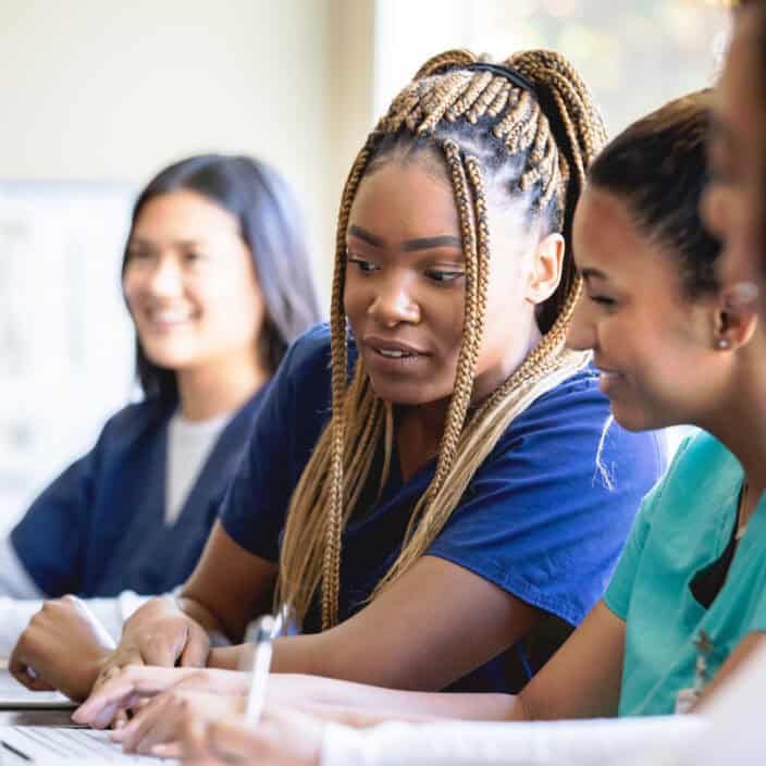 Diverse nursing students studying together with laptop in medical education classroom