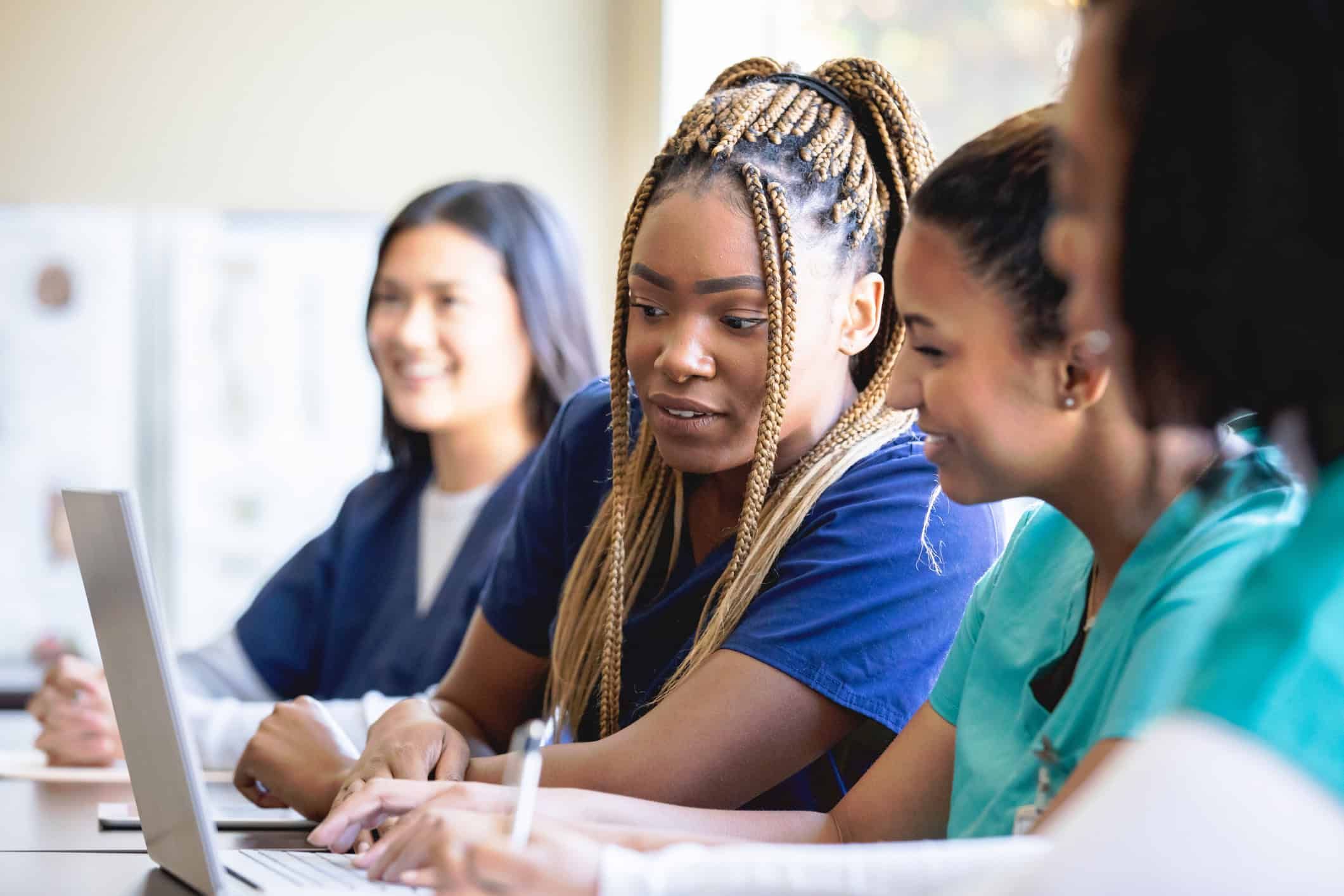 Diverse nursing students studying together with laptop in medical education classroom