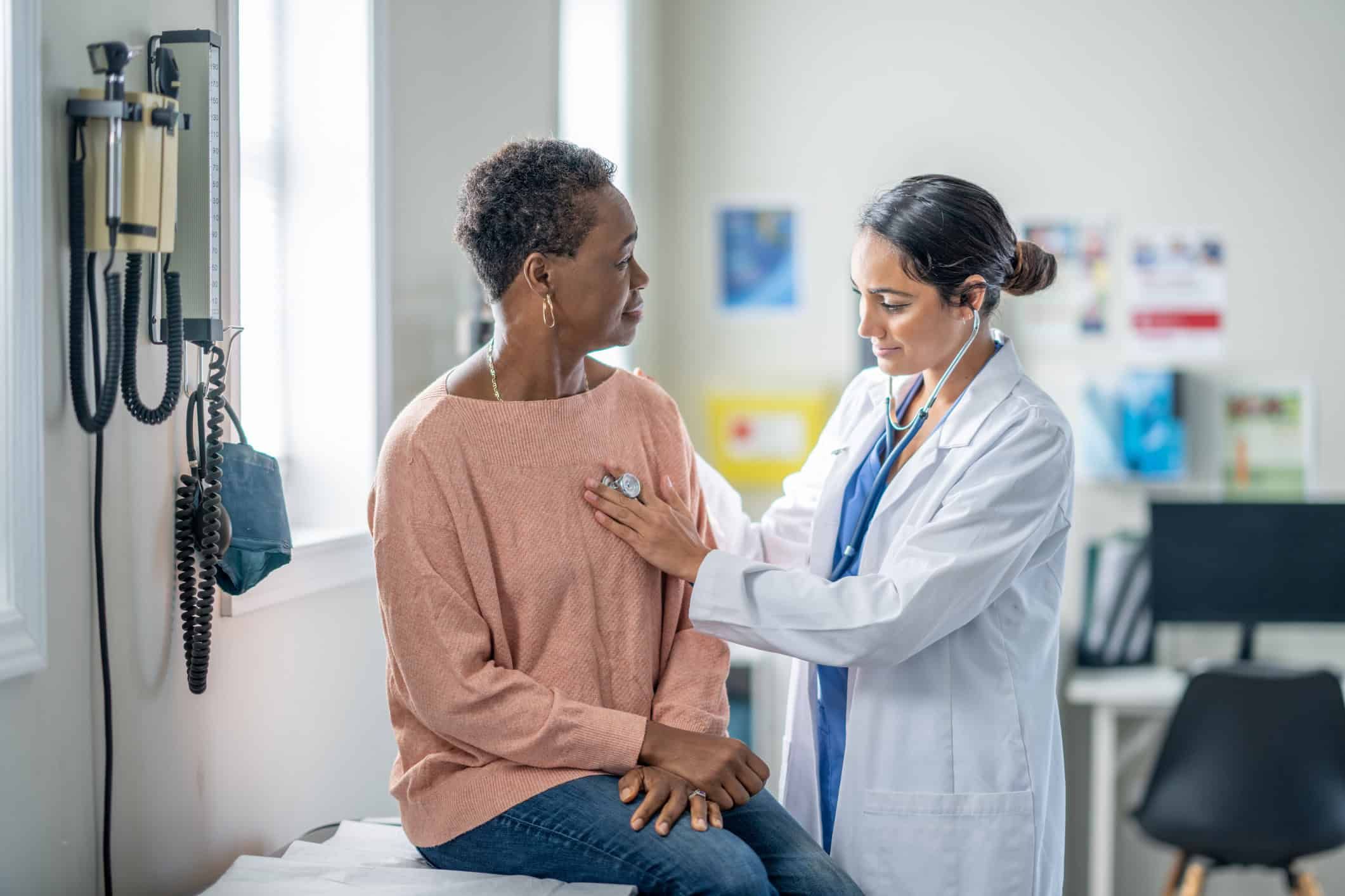 Doctor examining senior woman patient with stethoscope in medical office
