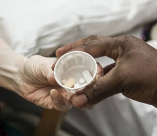 Nurse's hands giving medication pills in small cup to patient's outstretched hand
