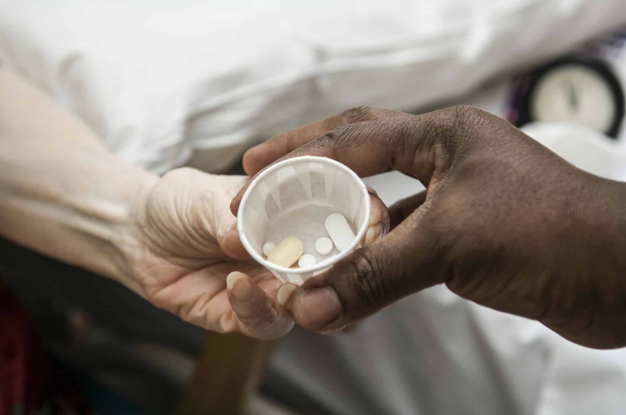 Nurse's hands giving medication pills in small cup to patient's outstretched hand