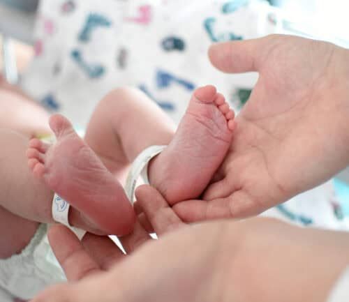 Parent gently cradling newborn baby's tiny feet in cupped hands
