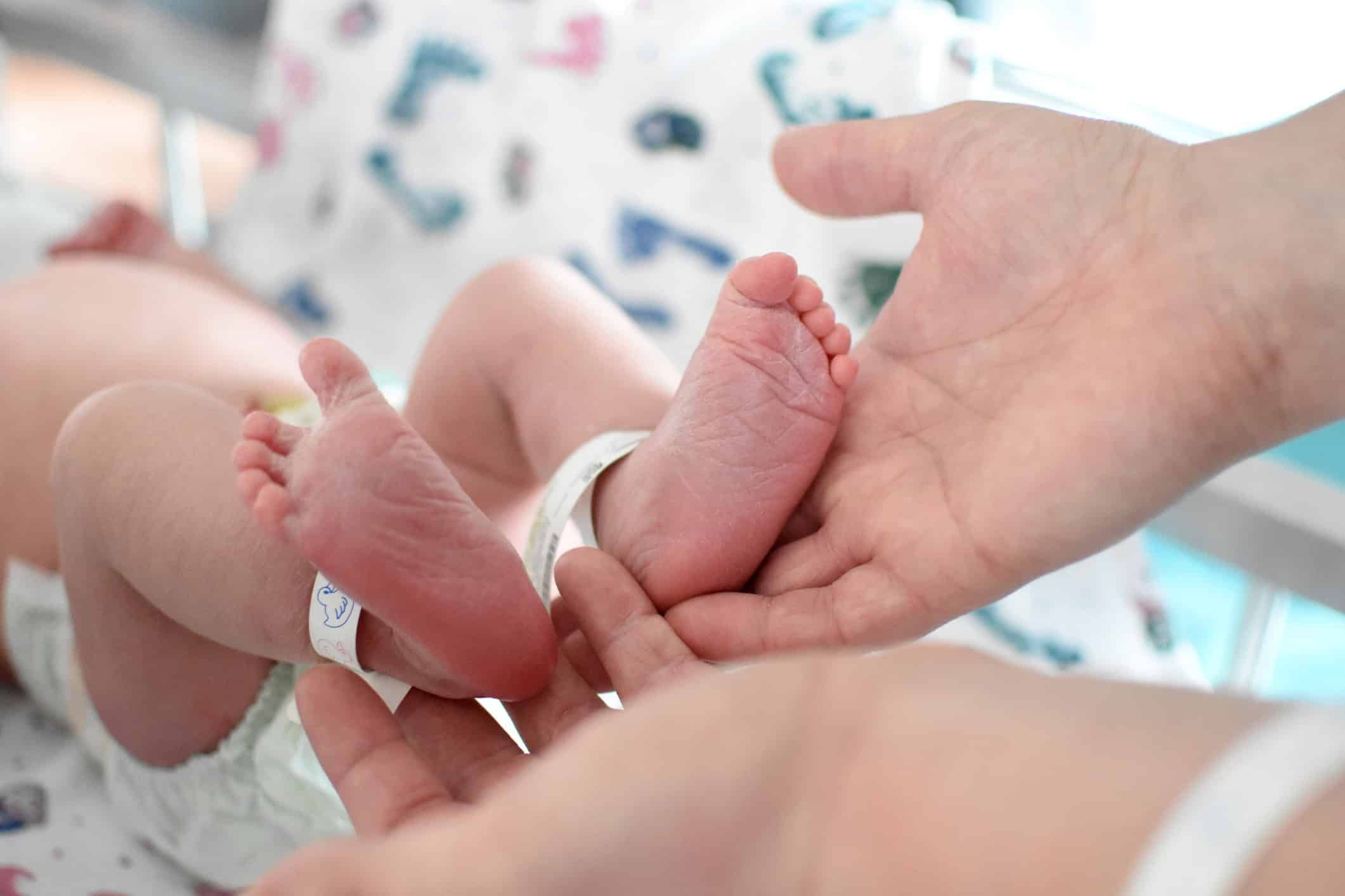 Parent gently cradling newborn baby's tiny feet in cupped hands