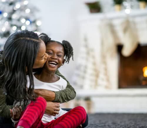 Mother kissing young daughter's cheek while embracing in cozy holiday home setting
