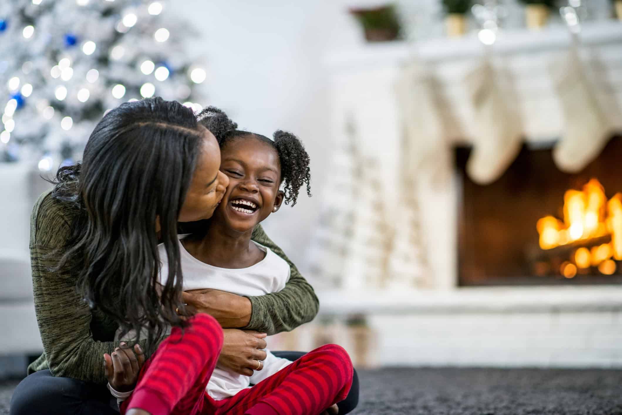Mother kissing young daughter's cheek while embracing in cozy holiday home setting