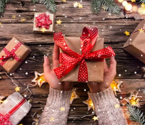 Woman's hands holding wrapped gift box with red ribbon on wooden table