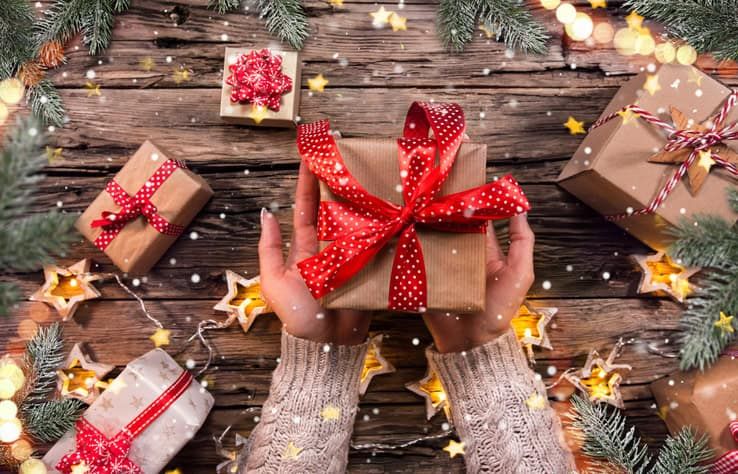 Woman's hands holding wrapped gift box with red ribbon on wooden table
