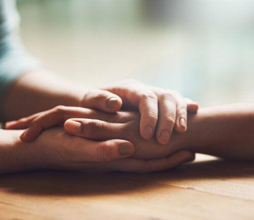 Two people holding hands on wooden surface showing comfort and support