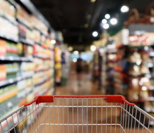 Shopping cart in grocery store aisle with blurred shelves and products in background