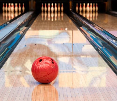 Red bowling ball on polished lane with pins at end