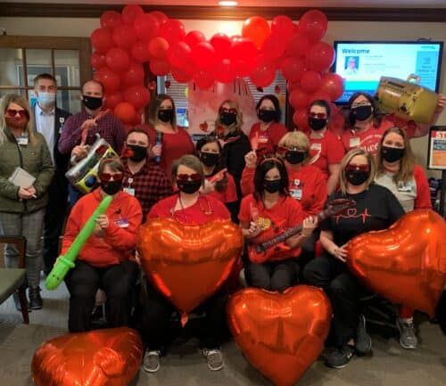 Healthcare staff wearing red and masks celebrate with heart balloons and decorations