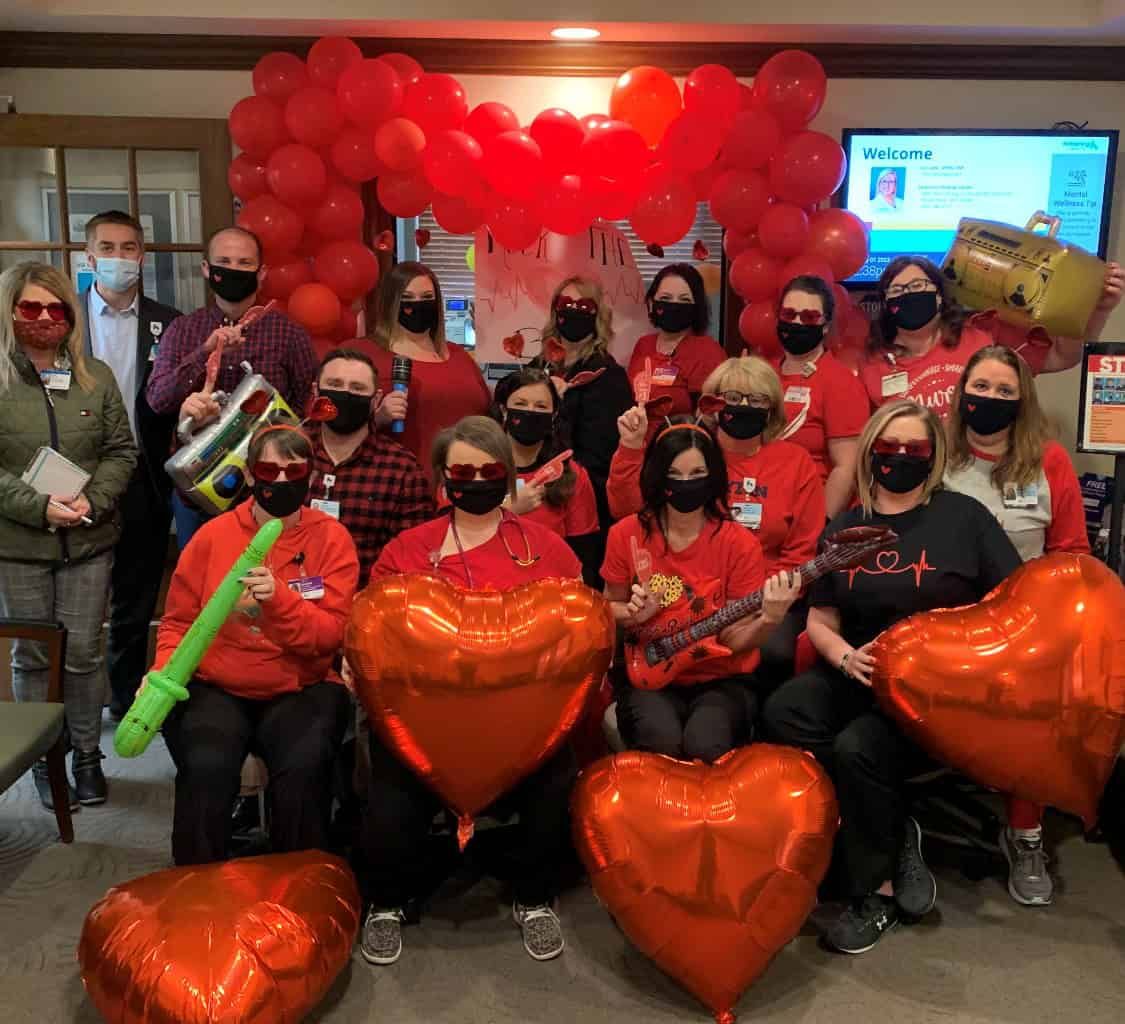Healthcare staff wearing red and masks celebrate with heart balloons and decorations