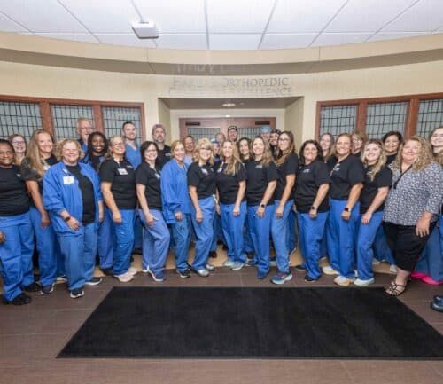 Large group of healthcare staff in blue scrubs posing together in medical facility lobby
