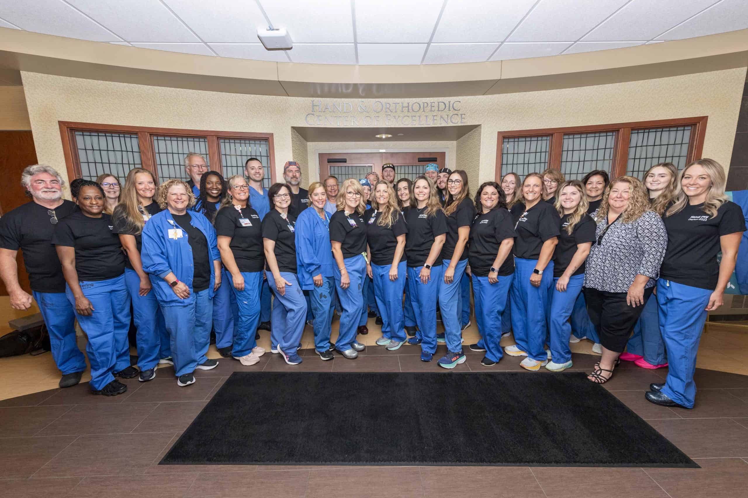 Large group of healthcare staff in blue scrubs posing together in medical facility lobby