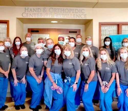 Medical staff in scrubs and masks posing together at Hand & Orthopedic Center of Excellence
