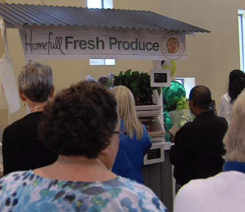 Customers shopping for fresh produce at Homefull market display with overhead signage