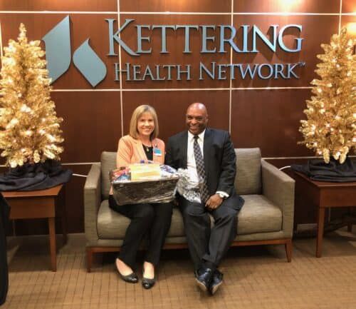 Two professionals sitting on couch with gift basket in Kettering Health lobby