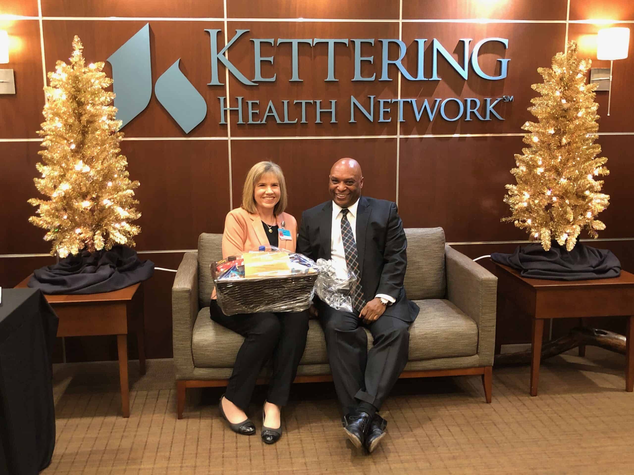 Two professionals sitting on couch with gift basket in Kettering Health lobby