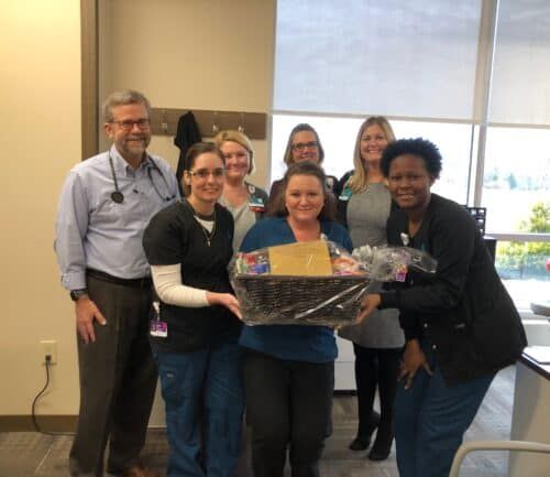 Healthcare team presenting gift basket to colleague in medical office setting