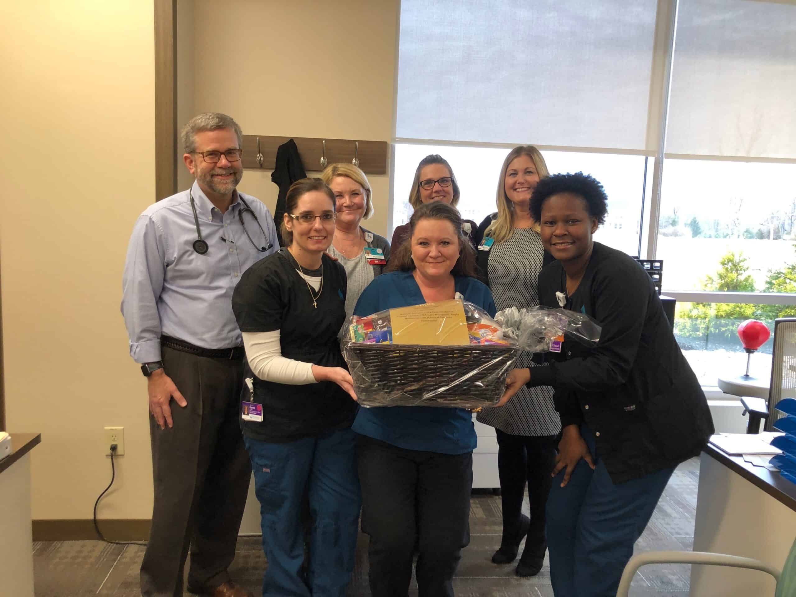 Healthcare team presenting gift basket to colleague in medical office setting