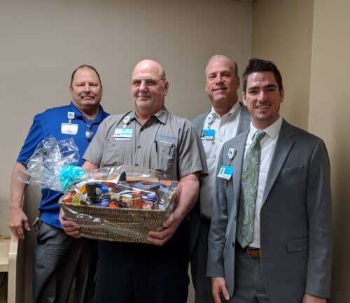 Four healthcare professionals posing together, one holding a gift basket presentation