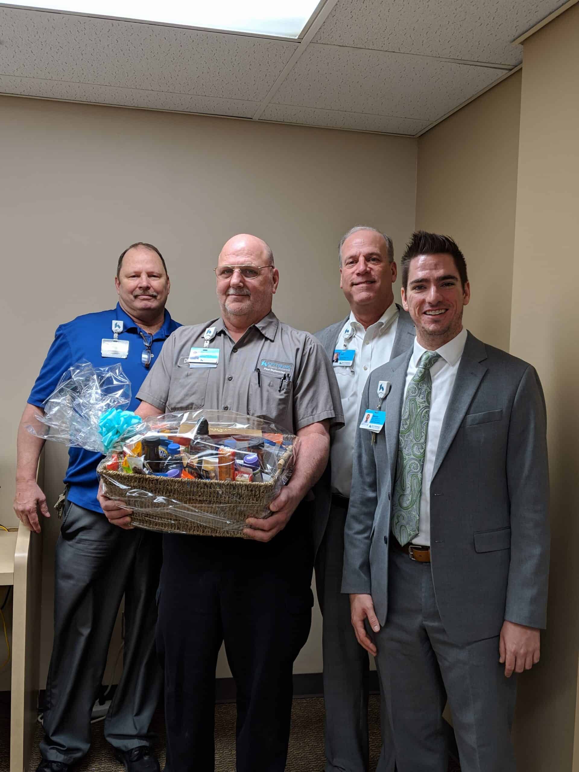 Four healthcare professionals posing together, one holding a gift basket presentation