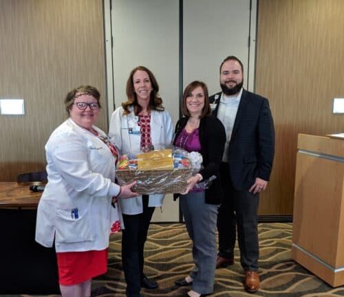 Four healthcare professionals posing together holding a gift basket in hospital lobby