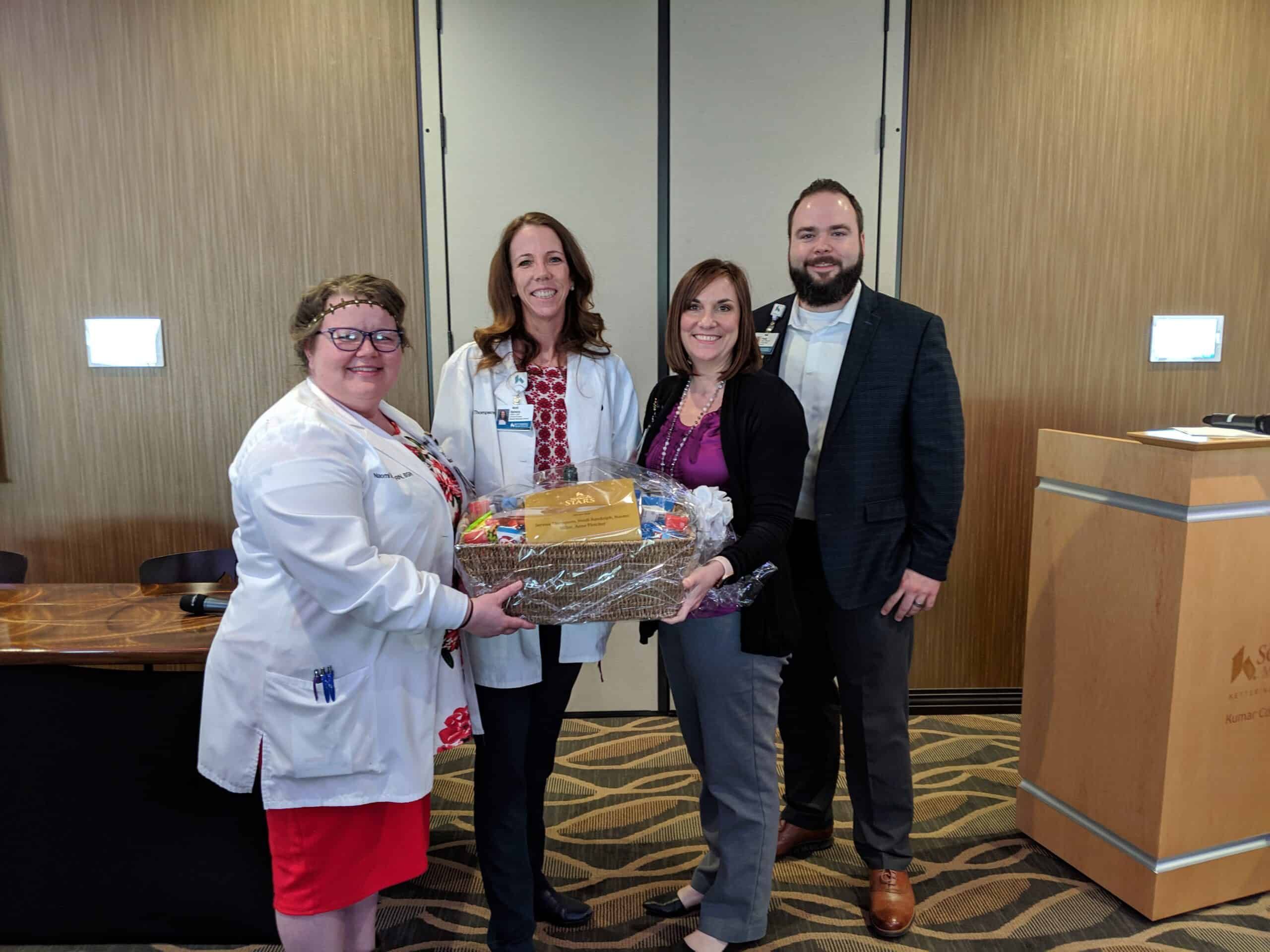 Four healthcare professionals posing together holding a gift basket in hospital lobby