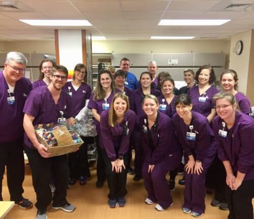 Healthcare team in purple scrubs celebrating with gift basket in hospital setting
