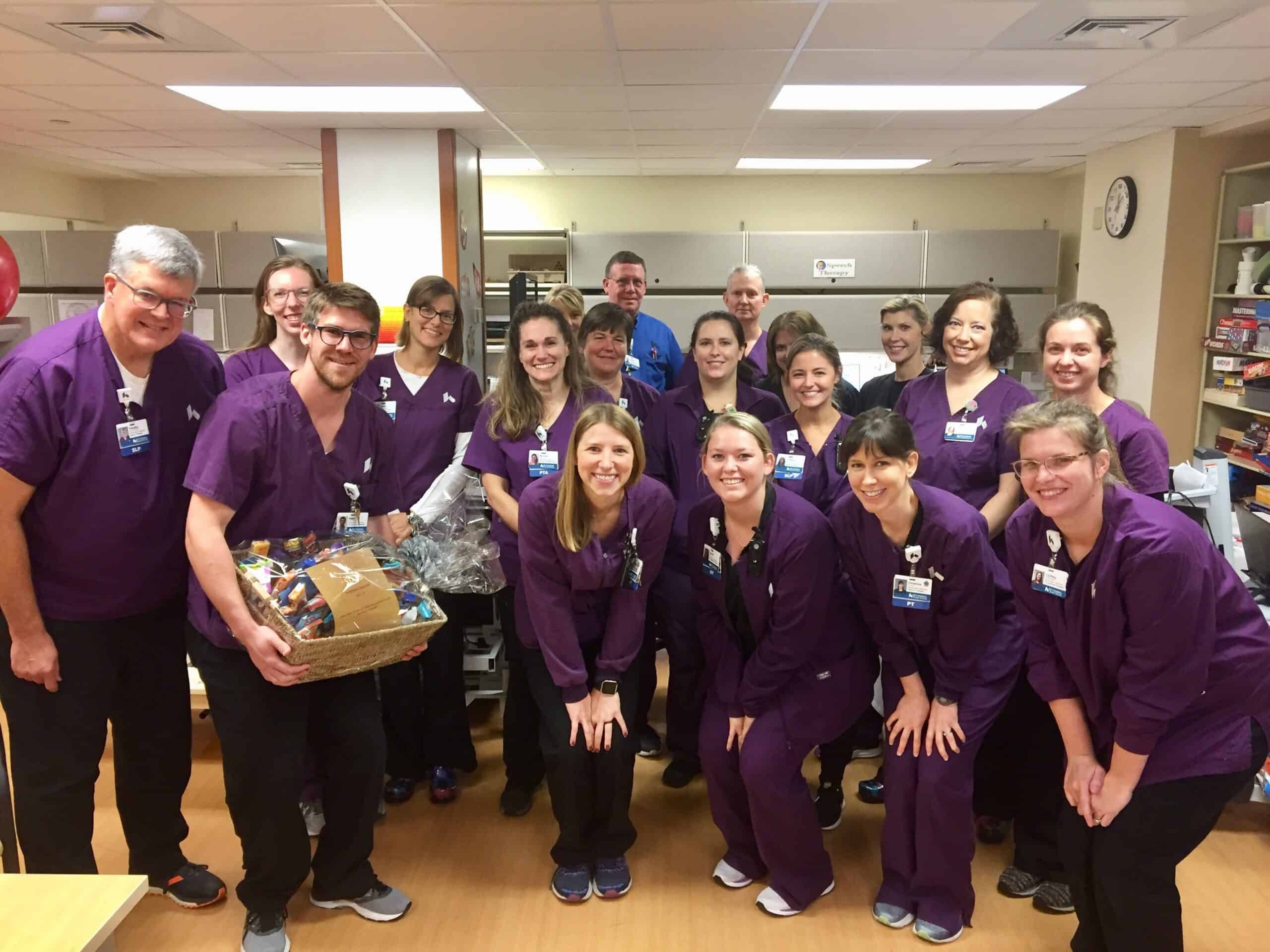 Healthcare team in purple scrubs celebrating with gift basket in hospital setting