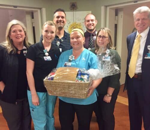 Healthcare team celebrating with employee holding gift basket in hospital hallway