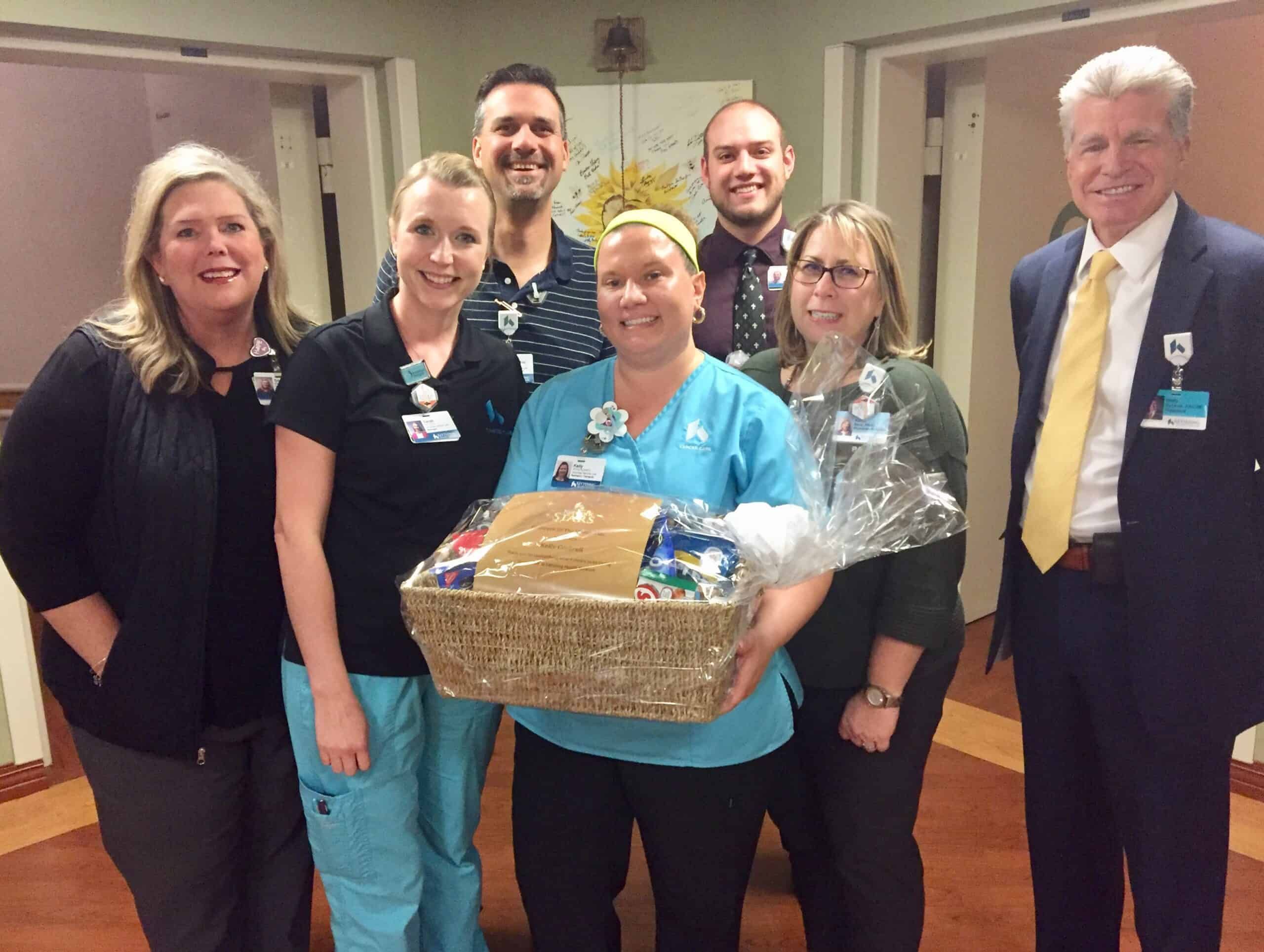 Healthcare team celebrating with employee holding gift basket in hospital hallway