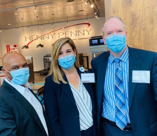 Three healthcare professionals wearing masks posing together in medical facility lobby