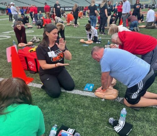 CPR training session on football field with instructor demonstrating chest compressions technique