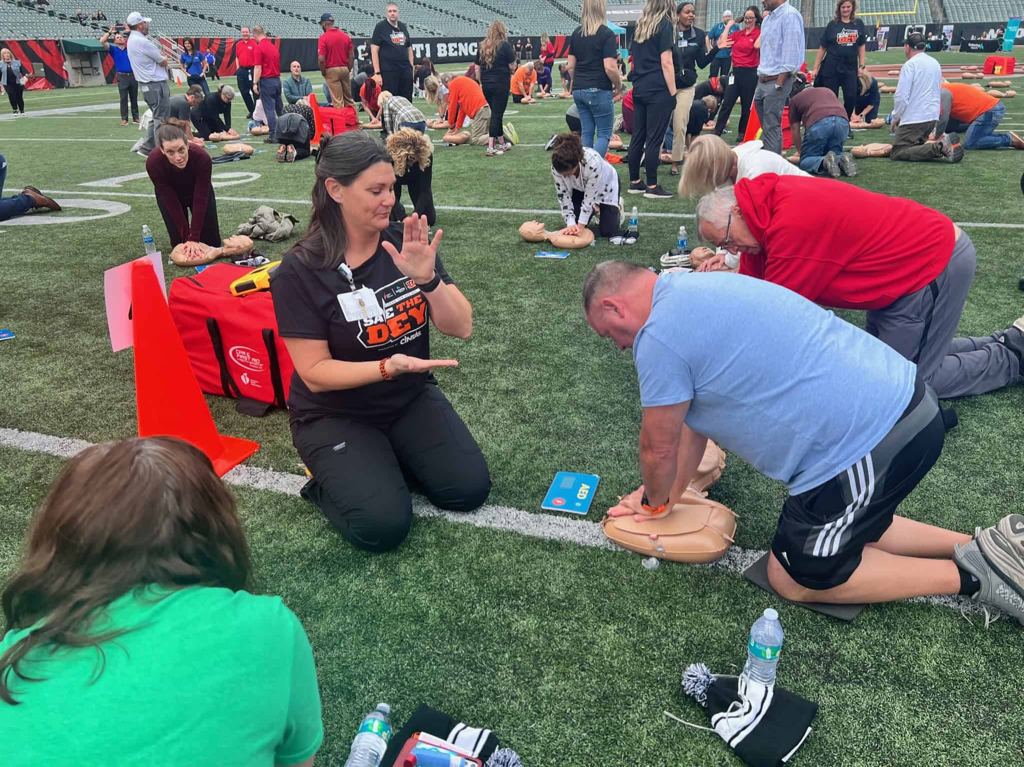 CPR training session on football field with instructor demonstrating chest compressions technique