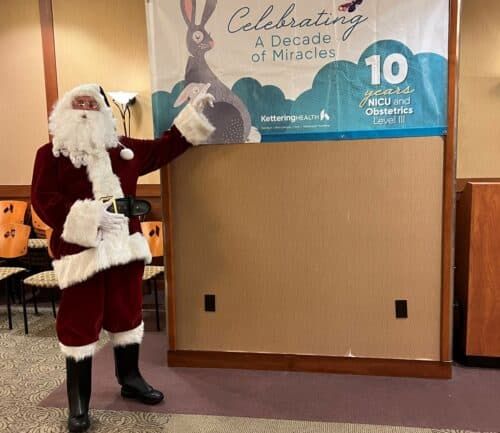 Santa Claus pointing at Kettering Health NICU anniversary banner celebrating decade of miracles