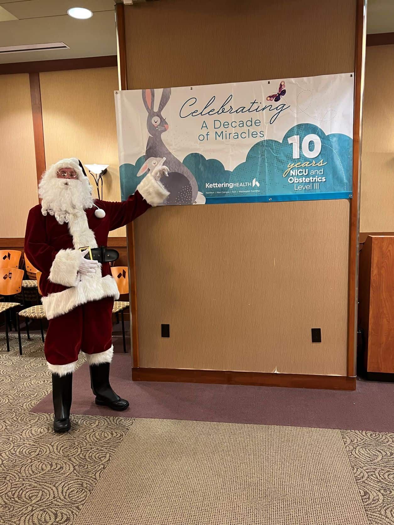 Santa Claus pointing at Kettering Health NICU anniversary banner celebrating decade of miracles
