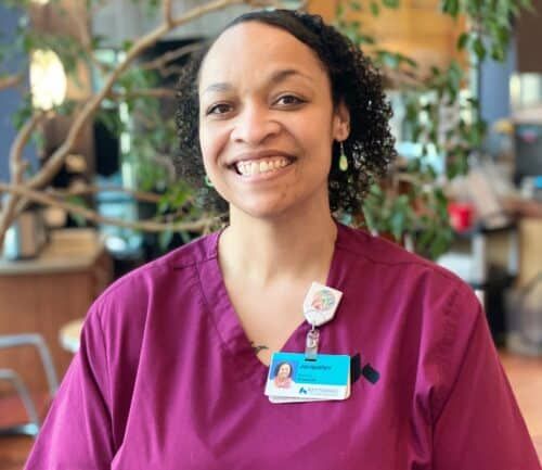 Healthcare professional in burgundy scrubs smiling in bright medical facility lobby