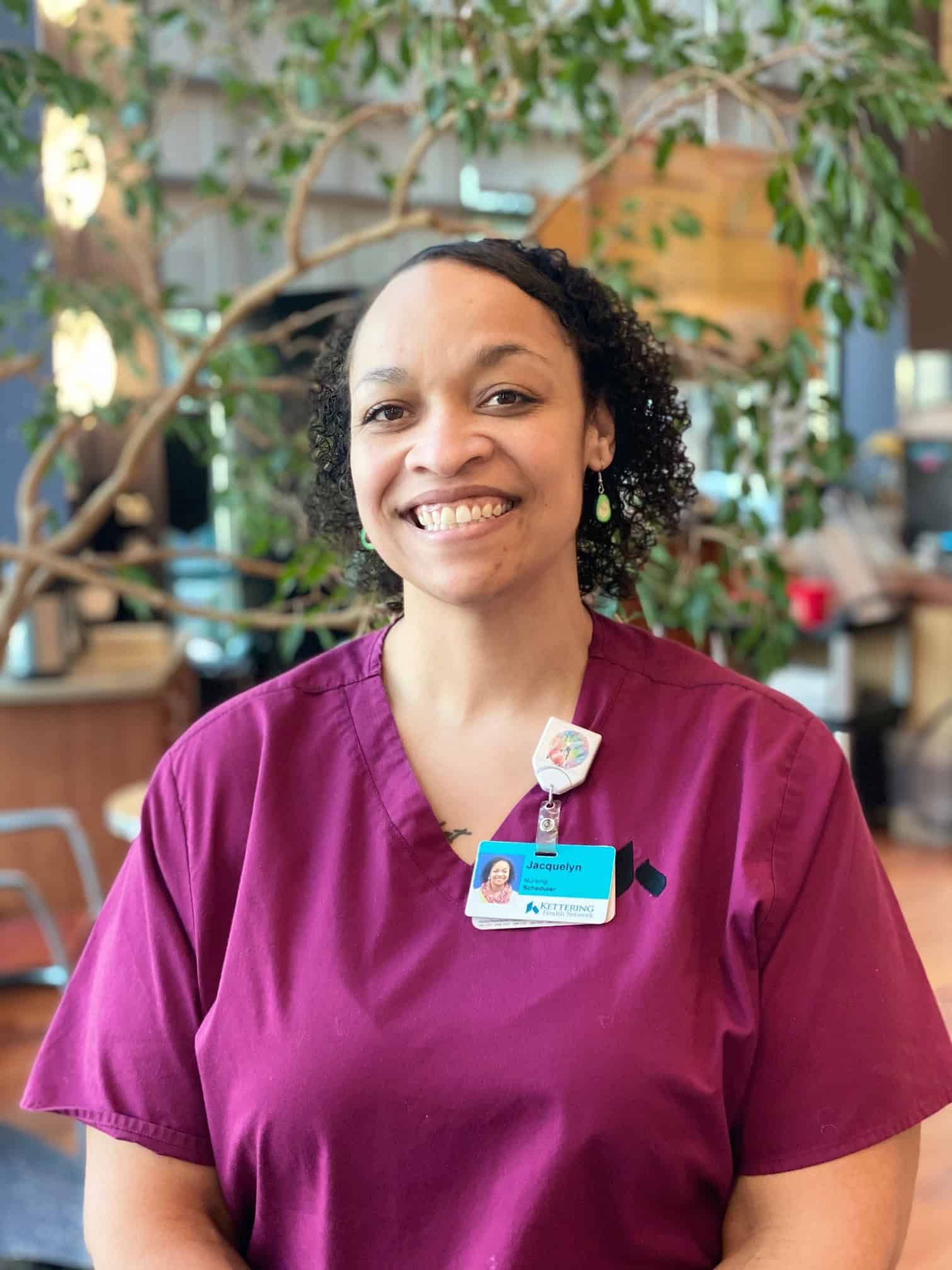 Healthcare professional in burgundy scrubs smiling in bright medical facility lobby