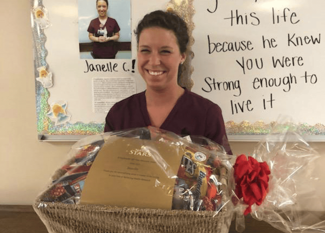 Healthcare worker Janelle holds gift basket with inspirational wall message behind her