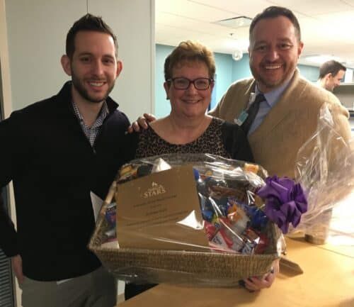 Three healthcare employees presenting award certificate and gift basket to smiling female recipient