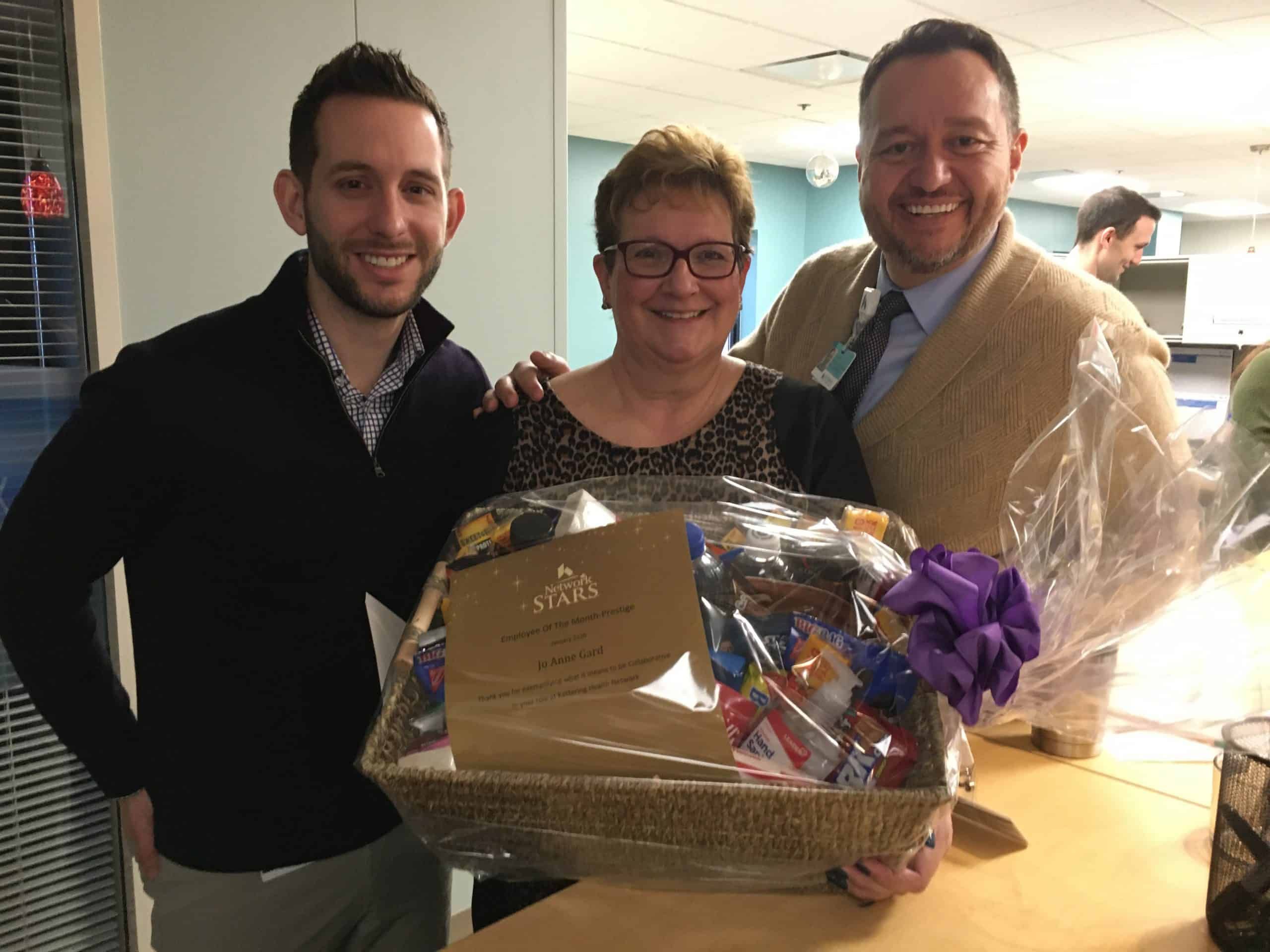 Three healthcare employees presenting award certificate and gift basket to smiling female recipient