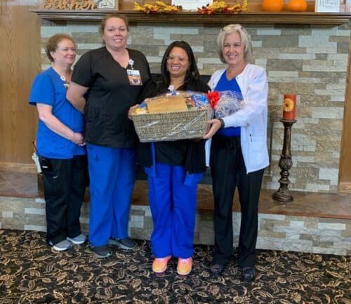Four healthcare workers presenting gift basket to colleague in hospital lobby