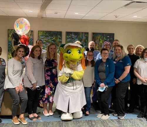 Healthcare team celebrates with dragon mascot and balloons in hospital setting