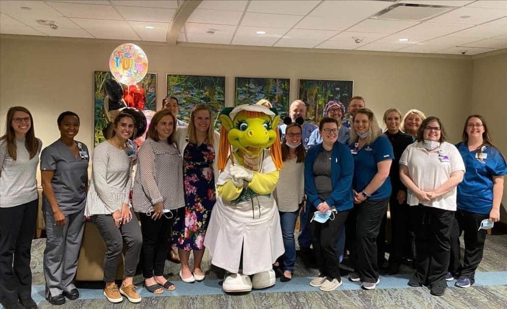 Healthcare team celebrates with dragon mascot and balloons in hospital setting