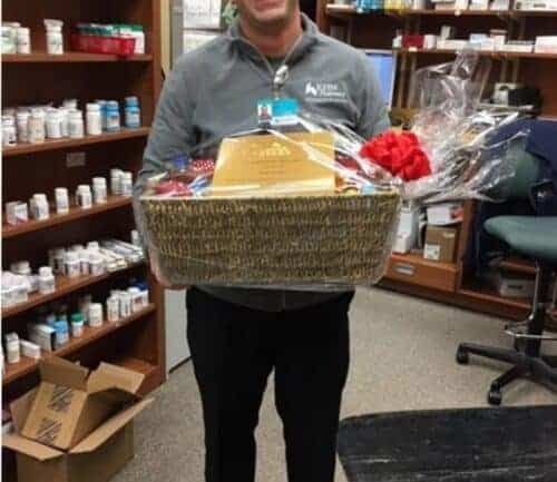 Healthcare professional holding gift basket in pharmacy with shelved medications behind him
