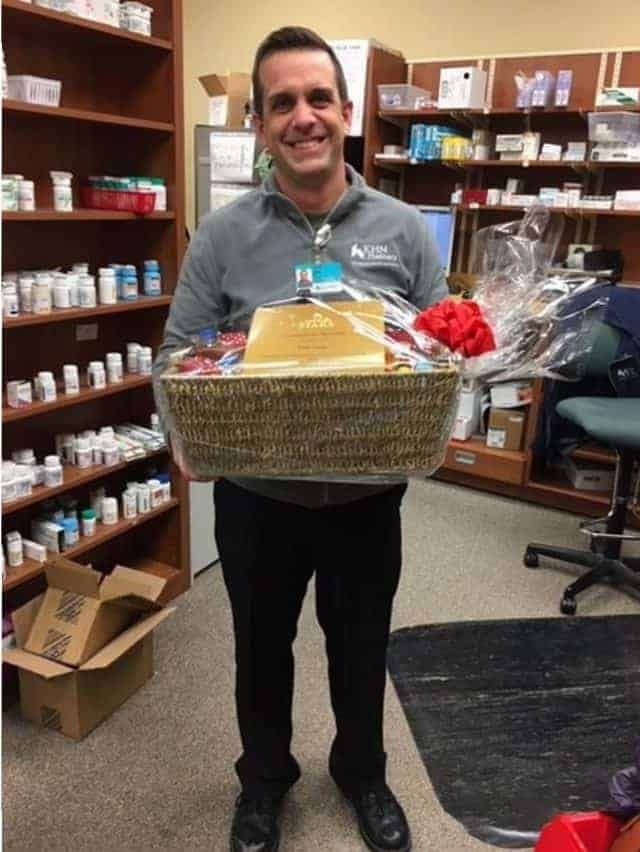 Healthcare professional holding gift basket in pharmacy with shelved medications behind him