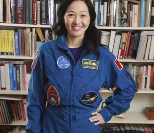 Professional headshot of Julielynn Wong in blue flight suit standing before bookshelf